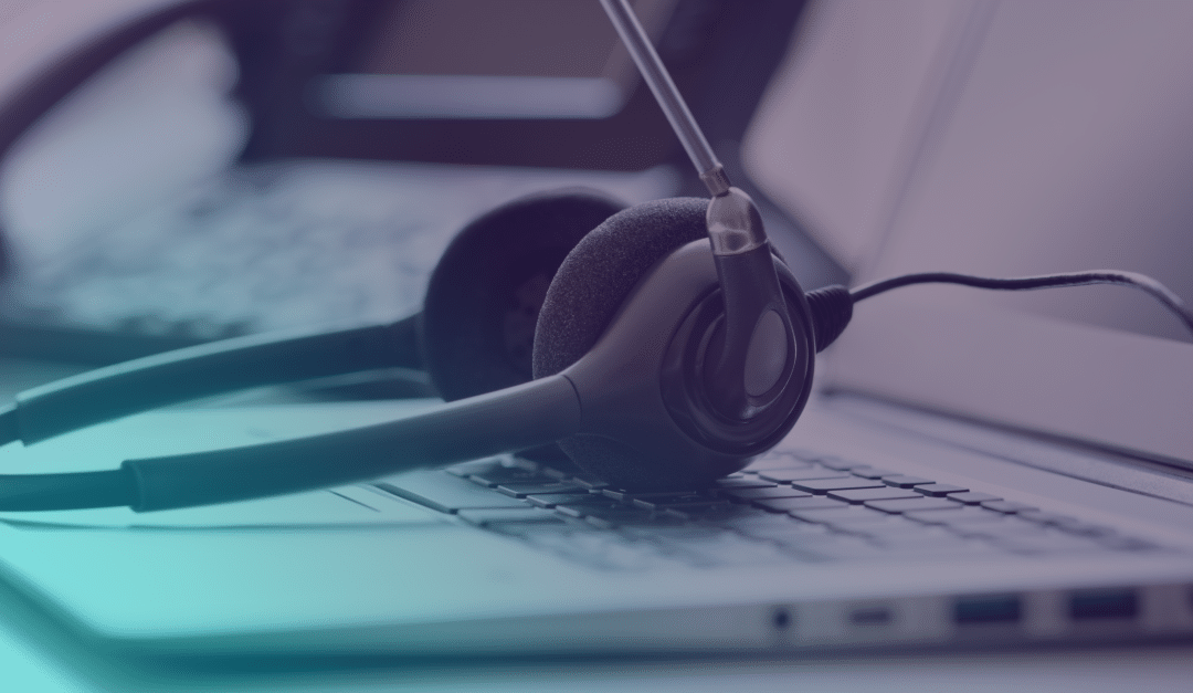 A black headset with a microphone rests on a laptop keyboard, with another laptop blurred in the background.