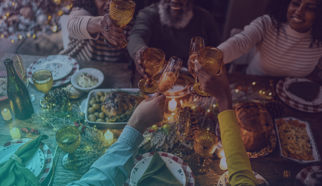 Seis personas brindan en torno a una mesa festiva decorada con velas, comida y plantas, creando un ambiente cálido y festivo.