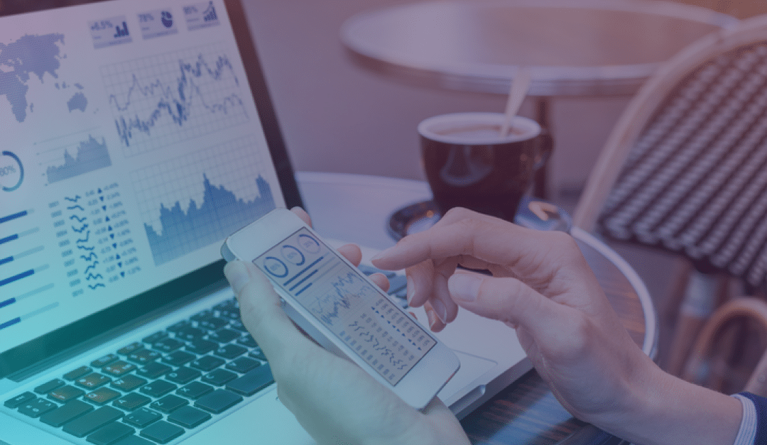Una persona revisa gráficos financieros en un smartphone y un portátil, sentada en la mesa de una cafetería con una taza de café, mostrando diversos gráficos y análisis de datos en ambos dispositivos.