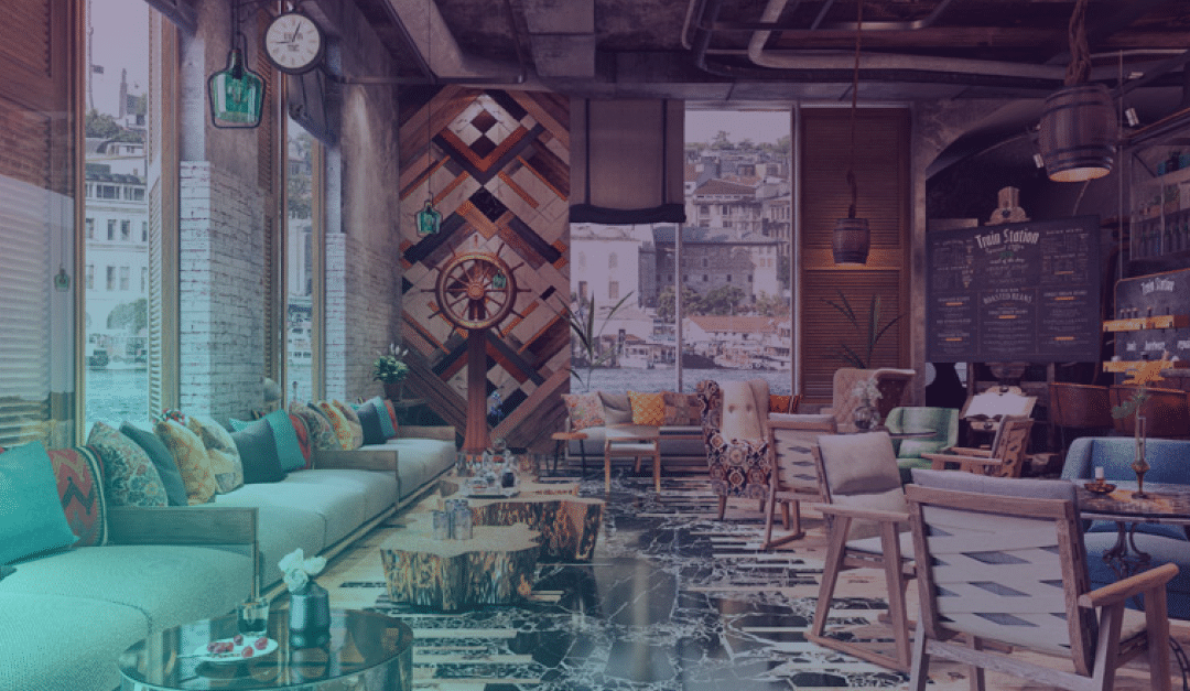 Interior de una cafetería colorida y ecléctica, con cojines estampados, mesas de madera, sillas modernas y cuadros en las paredes. Los grandes ventanales ofrecen unas vistas de la ciudad frente al mar. El suelo de mármol, las tuberías a la vista y la decoración acogedora crean un ambiente animado y acogedor.
