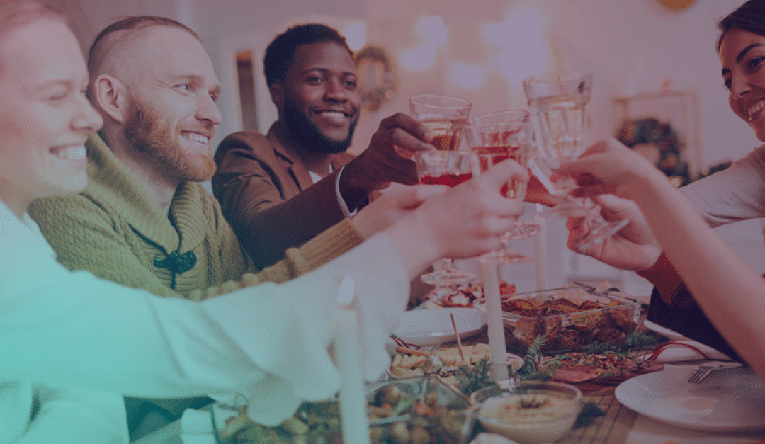 Cuatro personas sentadas alrededor de una mesa, sonriendo y levantando las copas para brindar, rodeadas de comida, velas y adornos festivos.