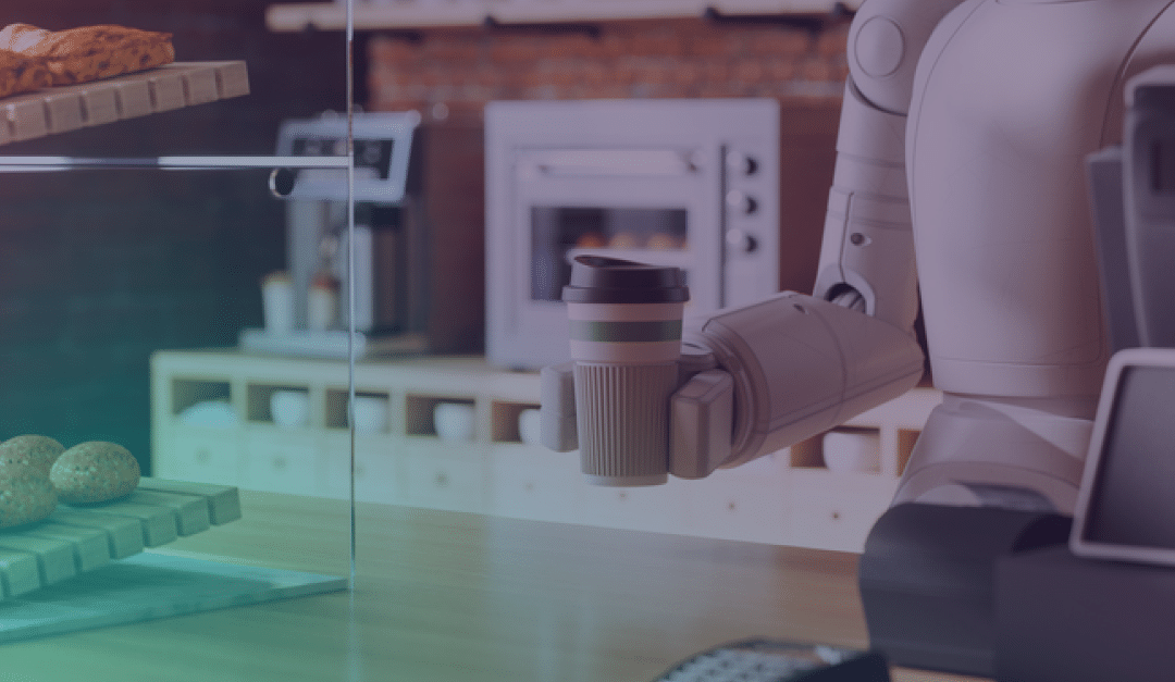 Un robot barista sostiene un vaso de café para llevar detrás del mostrador de una cafetería, donde se ven pasteles y una caja registradora, y un horno de ladrillo al fondo.