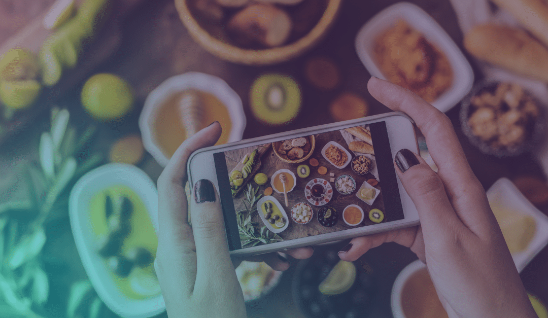 Una persona que está haciendo una foto con su smartphone de un colorido desayuno compuesto por diversos platos, frutas y bebidas dispuestos sobre una mesa.
