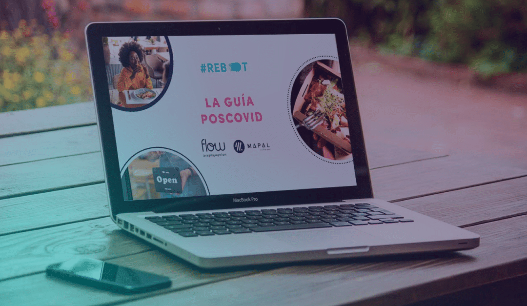 Un MacBook Pro, colocado sobre una mesa de madera, muestra una guía en español titulada «LA GUÍA POSCOVID», con imágenes de comida, una mujer y el letrero de una tienda. Junto al portátil hay un smartphone.