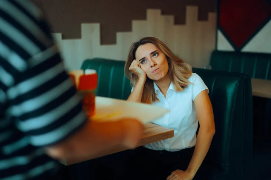 Una mujer sentada en una mesa de un restaurante no parece muy impresionada cuando un camarero se acerca con una bandeja de comida.