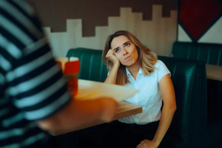 Una mujer sentada en una mesa de un restaurante no parece muy impresionada cuando un camarero se acerca con una bandeja de comida.