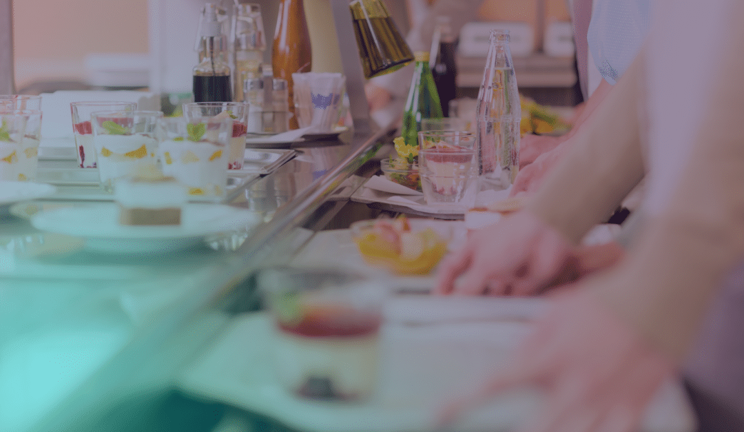 Des personnes munies de plateaux font la queue au comptoir d'une cafétéria, où elles choisissent leurs plats et leurs boissons. Divers desserts, salades et boissons sont présentés dans une vitrine.