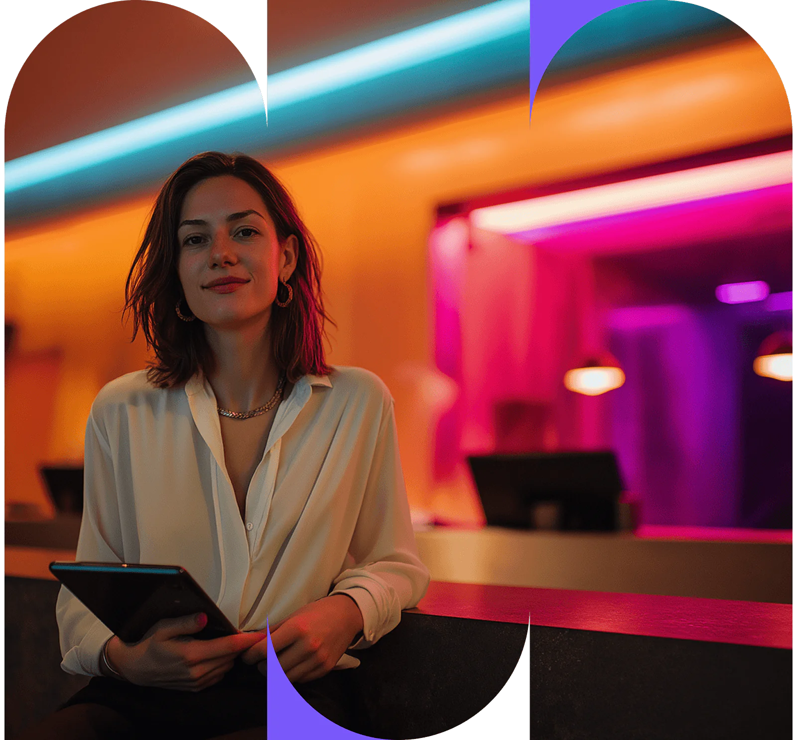 Uma mulher com uma blusa branca segura um tablet, sorrindo numa sala de estar moderna e colorida, com detalhes de iluminação em rosa néon, laranja e azul — pronta para lhe mostrar como aumentar a rentabilidade do seu hotel.