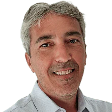 A middle-aged man with short grey hair, wearing a light-coloured collared shirt, smiling at the camera against a plain white background.