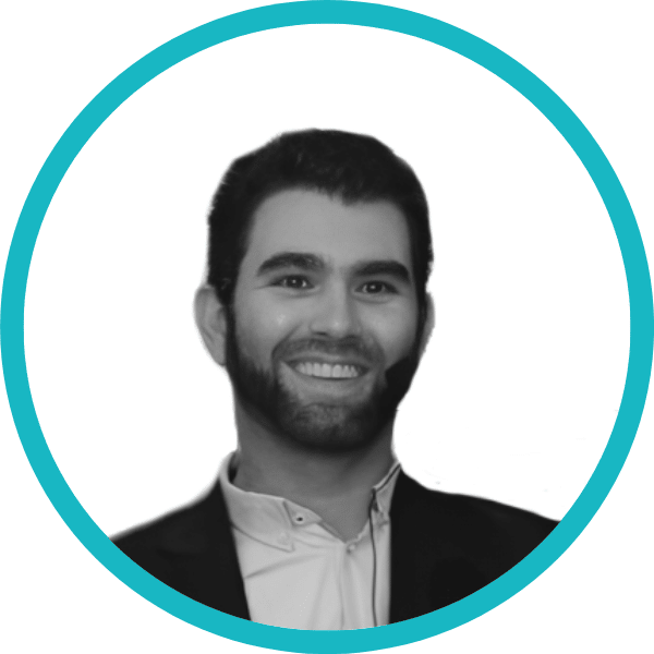 Black and white portrait of a man with dark hair and beard, smiling, wearing a suit jacket and light-coloured shirt, inside a turquoise circular frame on a white background.