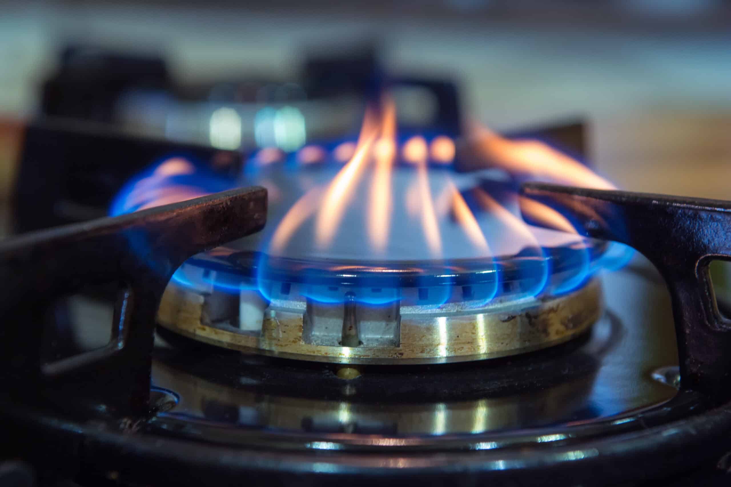 A close-up of a lit gas hob burner with blue and orange flames, surrounded by black metal grates.