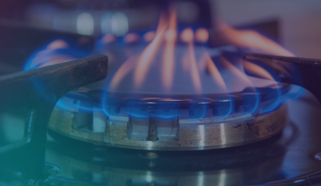 A close-up of a gas hob burner with a visible blue flame, showing metal pan supports and the circular burner head.