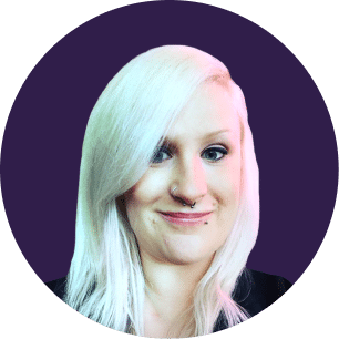A person with long, straight platinum blonde hair and facial piercings smiles at the camera. The background is a solid dark purple circle.