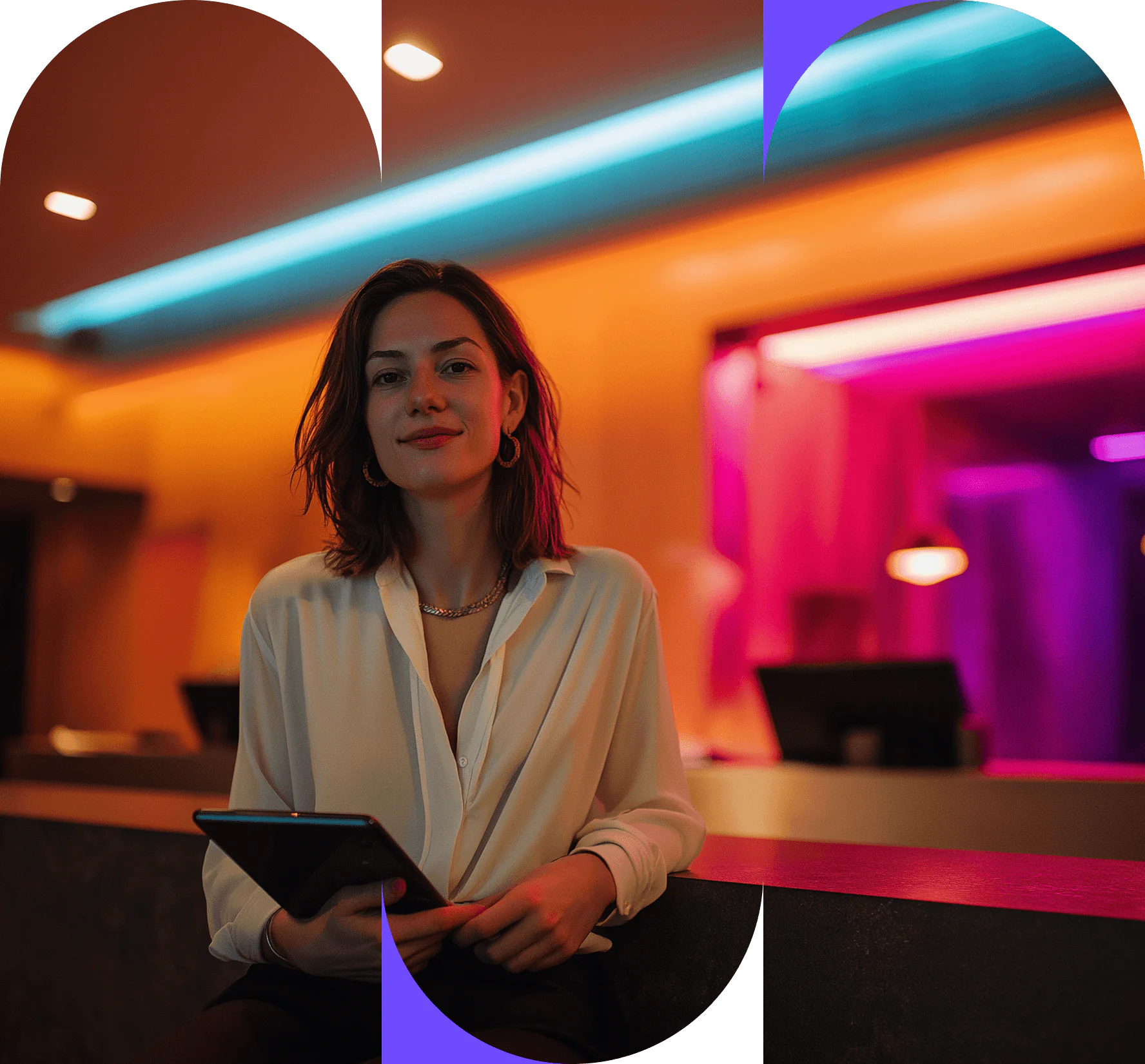 A woman in a white blouse holds a tablet whilst standing behind a reception desk in a room with blue and pink neon lighting, ready to implement strategies to improve hotel profitability.