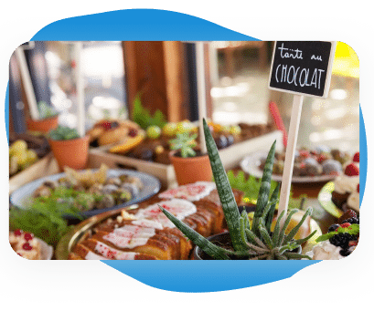 Une table de desserts proposant un assortiment de pâtisseries et de gâteaux, ainsi qu'une pancarte « tarte au chocolat », le tout agrémenté de plantes vertes et de plantes grasses.