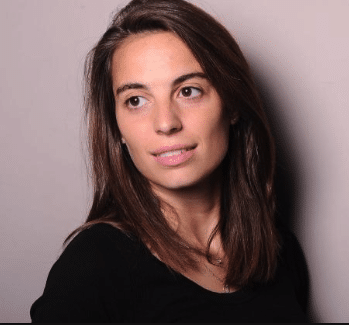 Une femme aux cheveux bruns raides, vêtue d'un haut noir, regarde légèrement vers sa gauche. Elle est photographiée devant un fond uni de couleur claire et affiche un léger sourire.