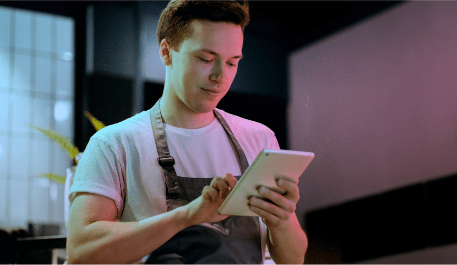 Une personne portant un tablier utilise une tablette, debout dans une pièce dont le décor est moderne.