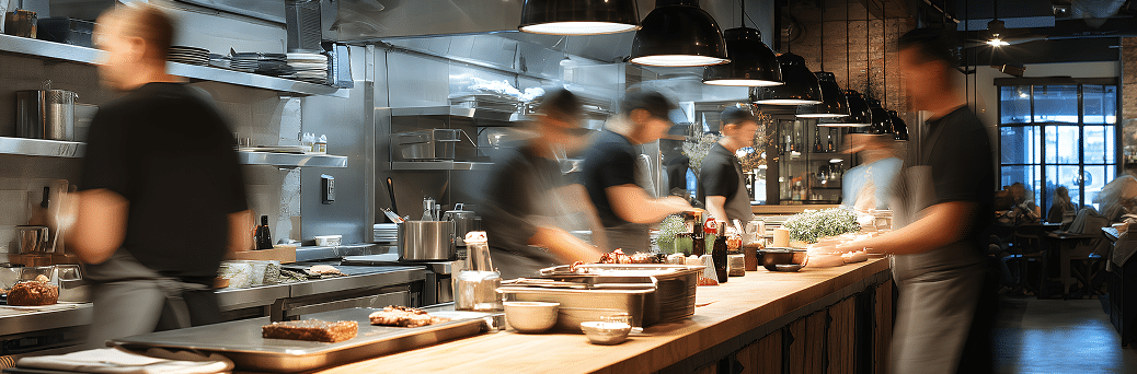 Una cocina de restaurante moderna y ajetreada, con cocineros que se mueven sin parar preparando platos en una larga barra de madera, electrodomésticos de acero inoxidable y lámparas negras colgantes.