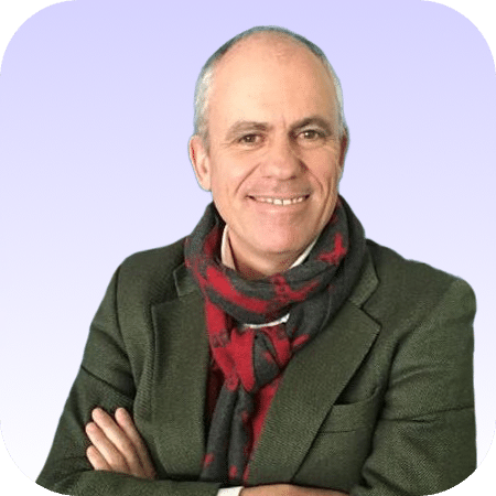 Un hombre de mediana edad, sonriente y con el pelo corto y canoso, que lleva una chaqueta verde y una bufanda roja y gris, aparece de pie con los brazos cruzados sobre un fondo morado claro.