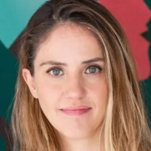 Una mujer con el pelo largo y castaño claro y los ojos azules mira a la cámara, esbozando una leve sonrisa. El fondo es colorido, con formas abstractas y siluetas en rojo y verde.