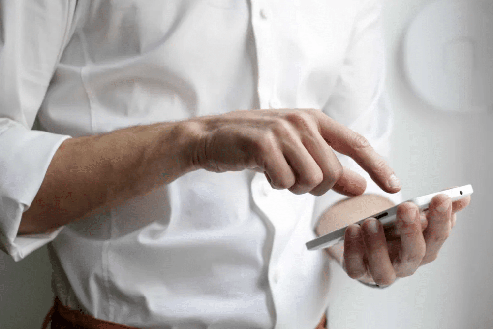 Una persona que lleva una camisa blanca está utilizando un smartphone: lo sostiene con una mano y toca la pantalla con la otra.