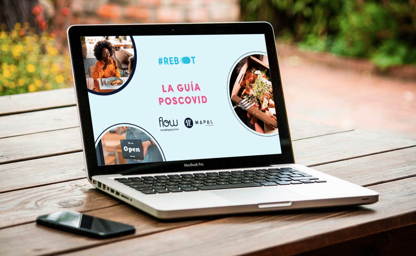 Un ordenador portátil, situado sobre una mesa de madera, muestra una pantalla en la que aparecen «La Guía Poscovid», imágenes de comida y logotipos. Junto al ordenador portátil hay un smartphone. El escenario parece estar al aire libre.