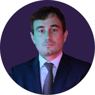 Un hombre vestido con traje oscuro y corbata posa sobre un fondo circular morado, con una iluminación verde y rosa que ilumina su rostro.