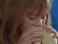 Una niña le da un gran mordisco a una hamburguesa, con aire concentrado mientras come.