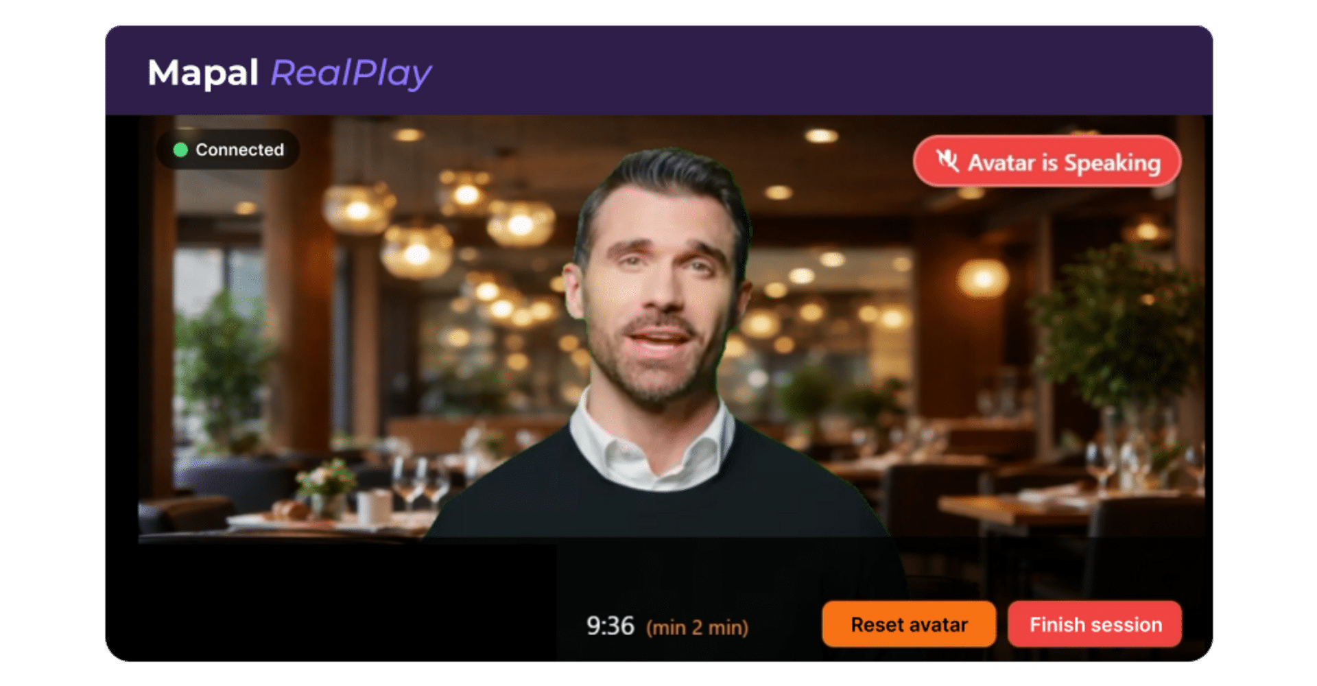 A man with short dark hair and a trimmed beard speaks during a virtual session, shown on a screen with options to reset avatar or finish session, and the text Avatar is Speaking highlighted in red.