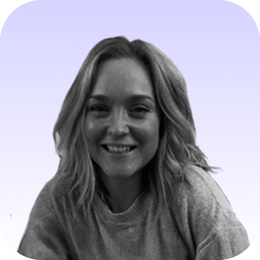 Black and white photo of a woman with shoulder-length wavy hair, smiling, wearing a sweatshirt. The background is a soft gradient of light purple to white with rounded corners on the image.