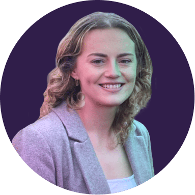 A woman with curly, shoulder-length hair, wearing a light grey blazer and a white top, smiles at the camera against a dark purple circular background.
